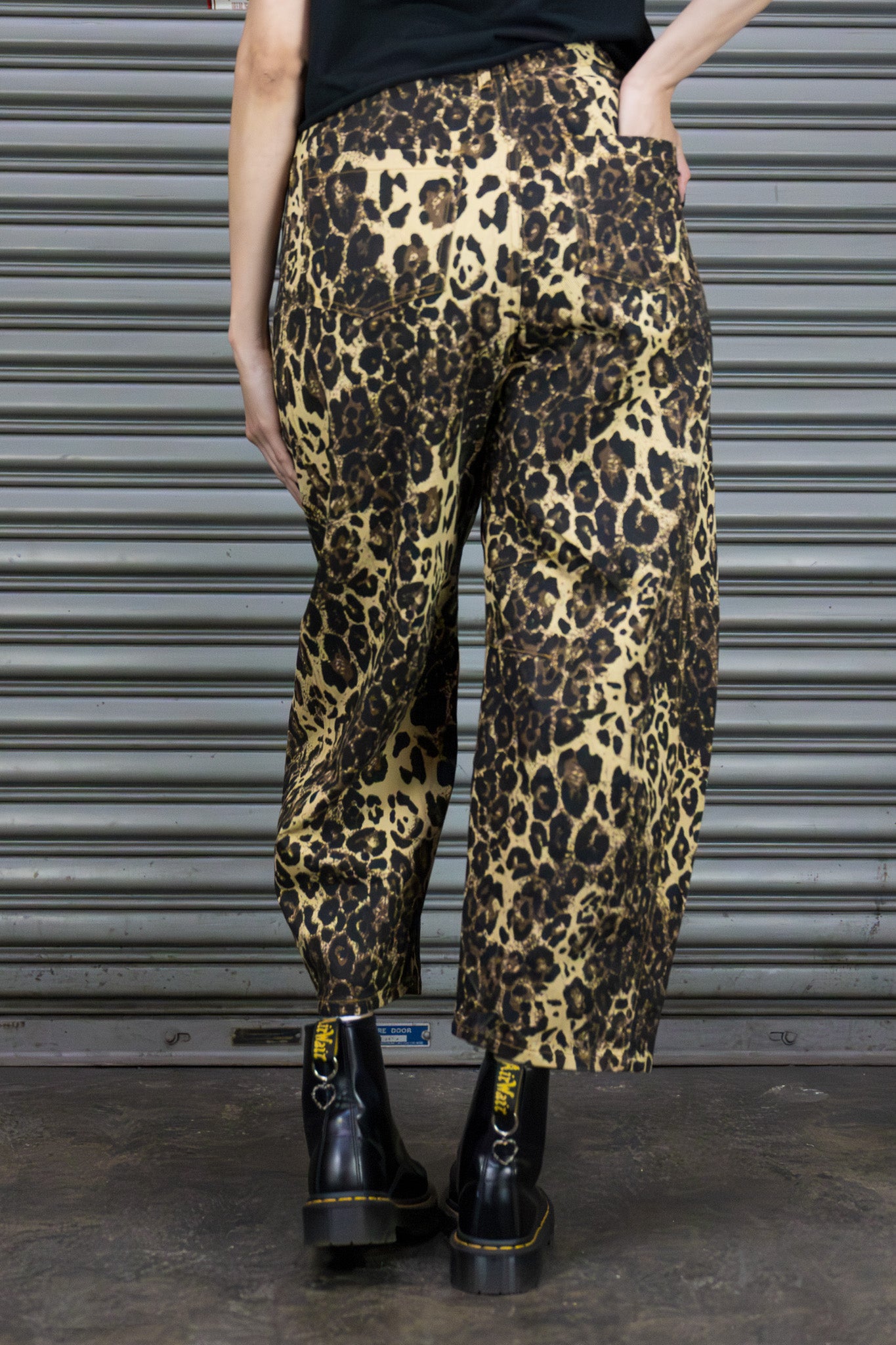 Person wearing leopard print pants and black boots in front of a metallic shutter.