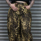 Person wearing leopard print pants and a black top against a metallic background