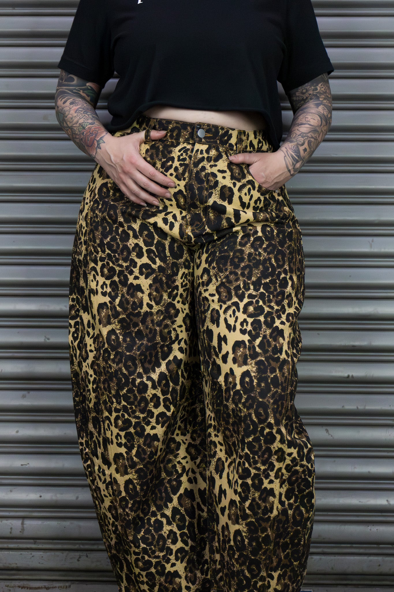 Person wearing leopard print pants and a black top against a metallic background