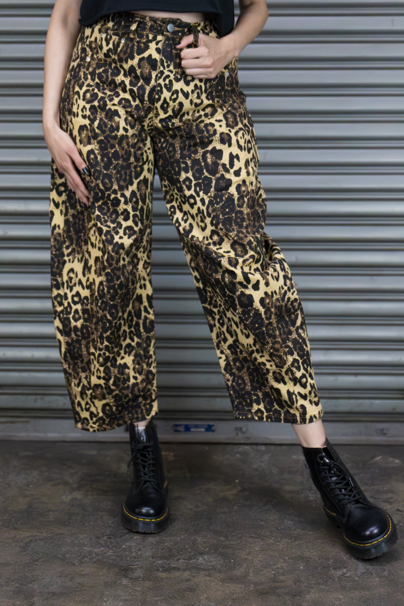 Person wearing leopard print pants and black boots standing in front of a metal shutter.