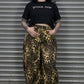 Person wearing a black t-shirt with text and leopard print pants standing in front of a metal shutter.