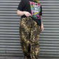 Person wearing a black graphic t-shirt and leopard print pants standing in front of a metal shutter.