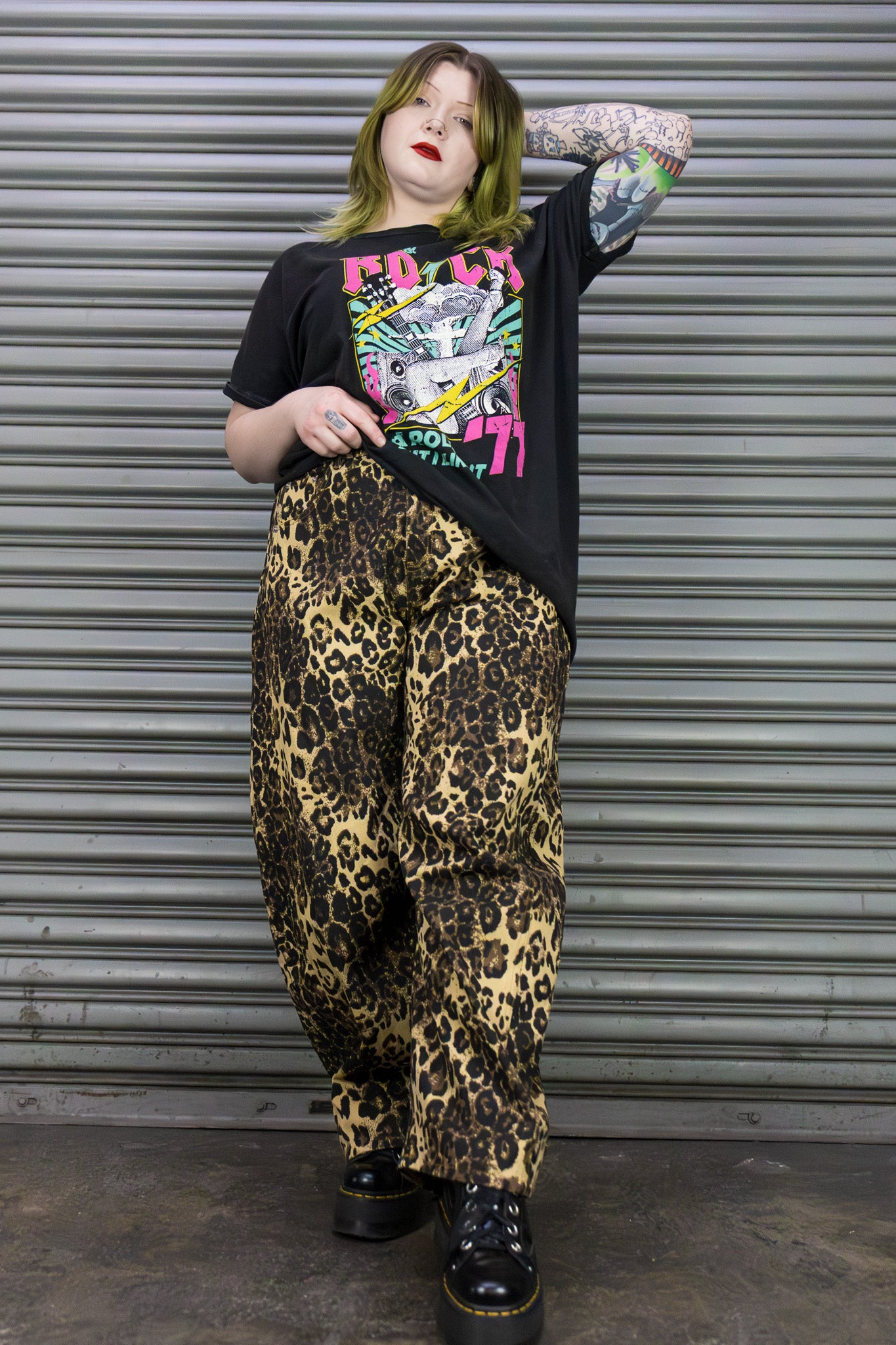 Person wearing a graphic t-shirt and leopard print pants standing in front of a metal shutter.