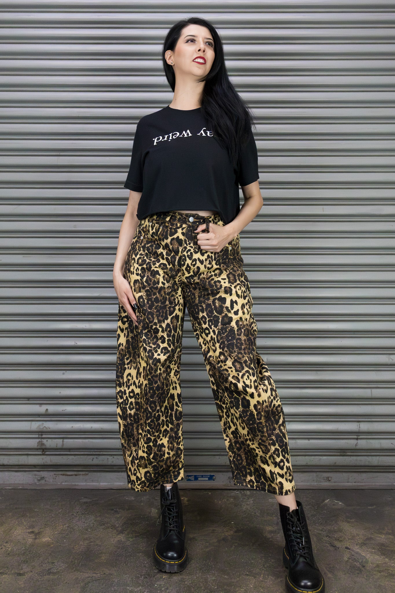 Woman wearing a black t-shirt and leopard print pants standing in front of a metallic shutter.