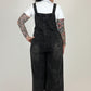 woman  wearing black denim overalls standing against a white backdrop