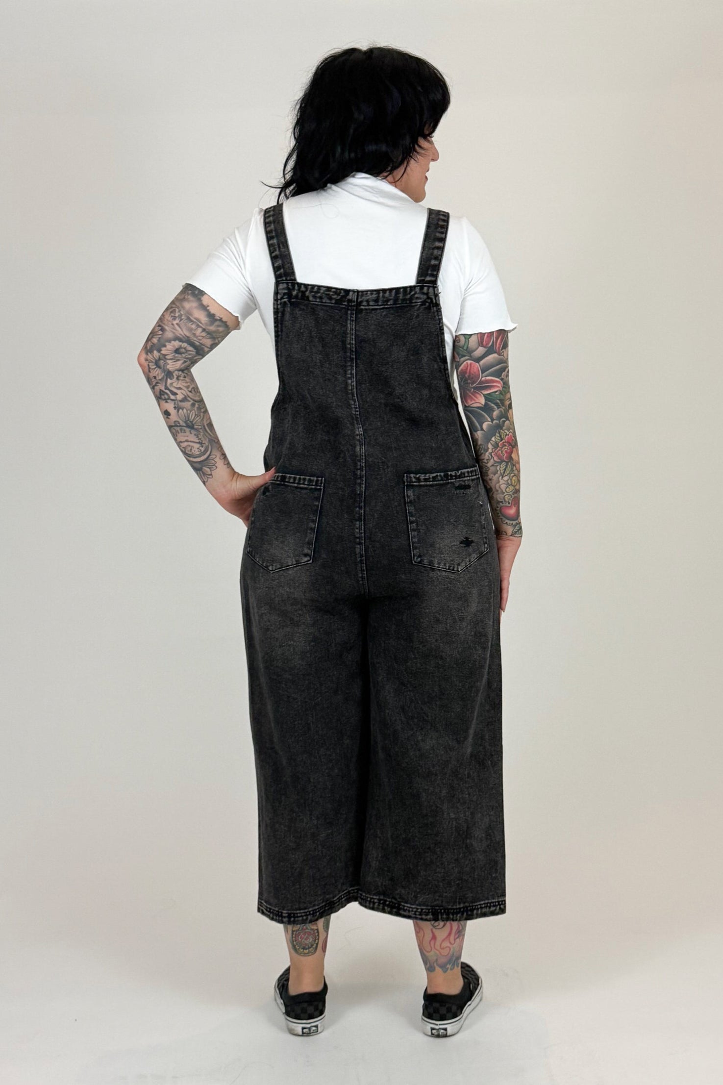 woman  wearing black denim overalls standing against a white backdrop