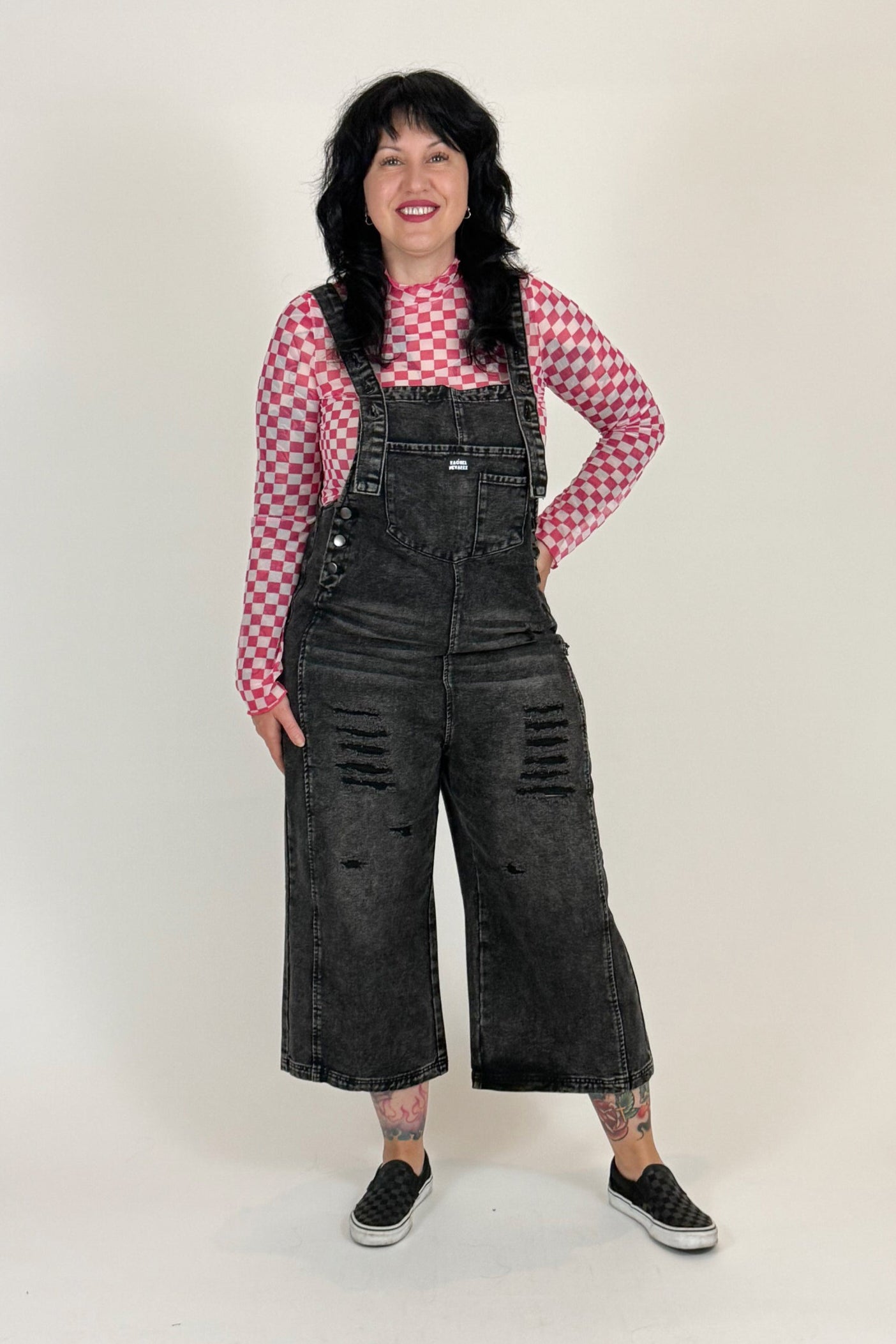 Person wearing black overalls and a red checkered shirt on a white background