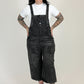 woman wearing black distressed overalls and a white t-shirt on a white background