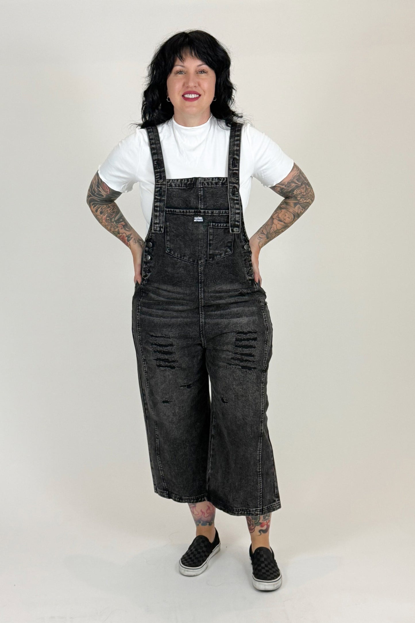 woman wearing black distressed overalls and a white t-shirt on a white background