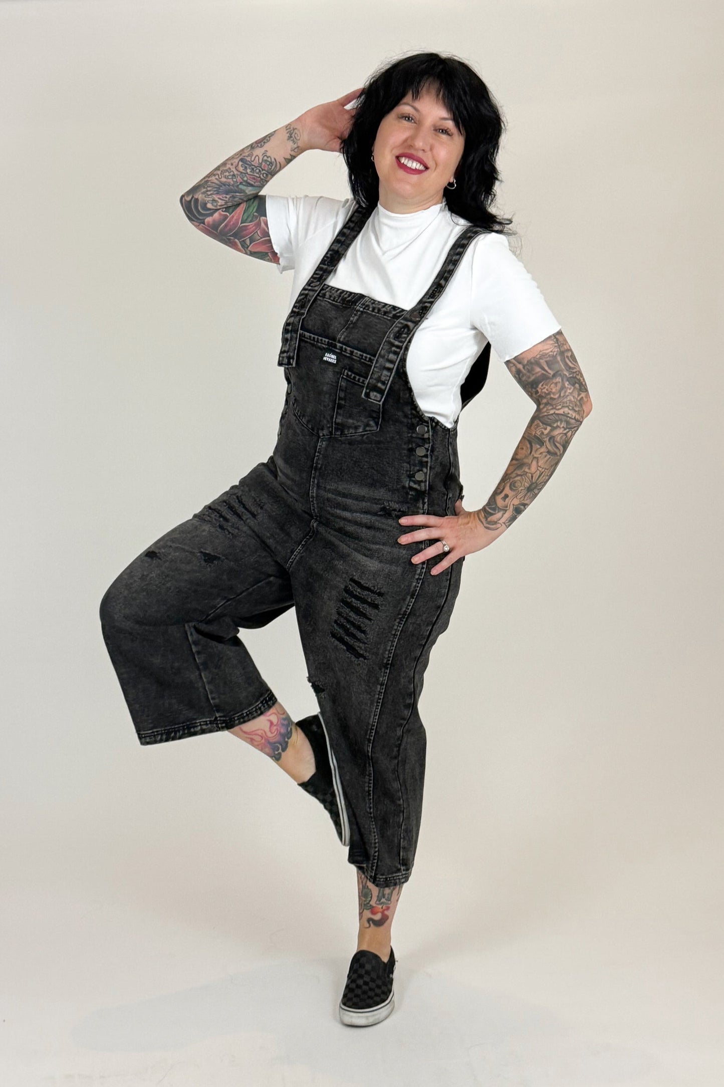Woman wearing black overalls and a white shirt on a white background