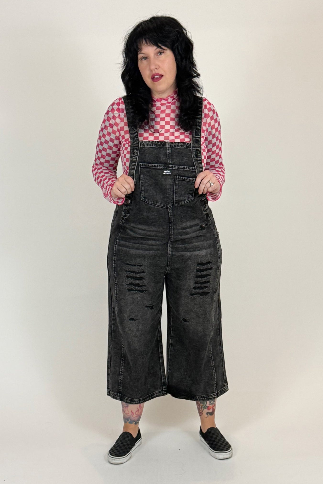 woman wearing black overalls and a pink checkered shirt on a white background