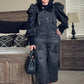 Person wearing a black denim overalls and black top in a bedroom setting.