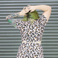 Person wearing a leopard print dress in front of a corrugated metal wall.