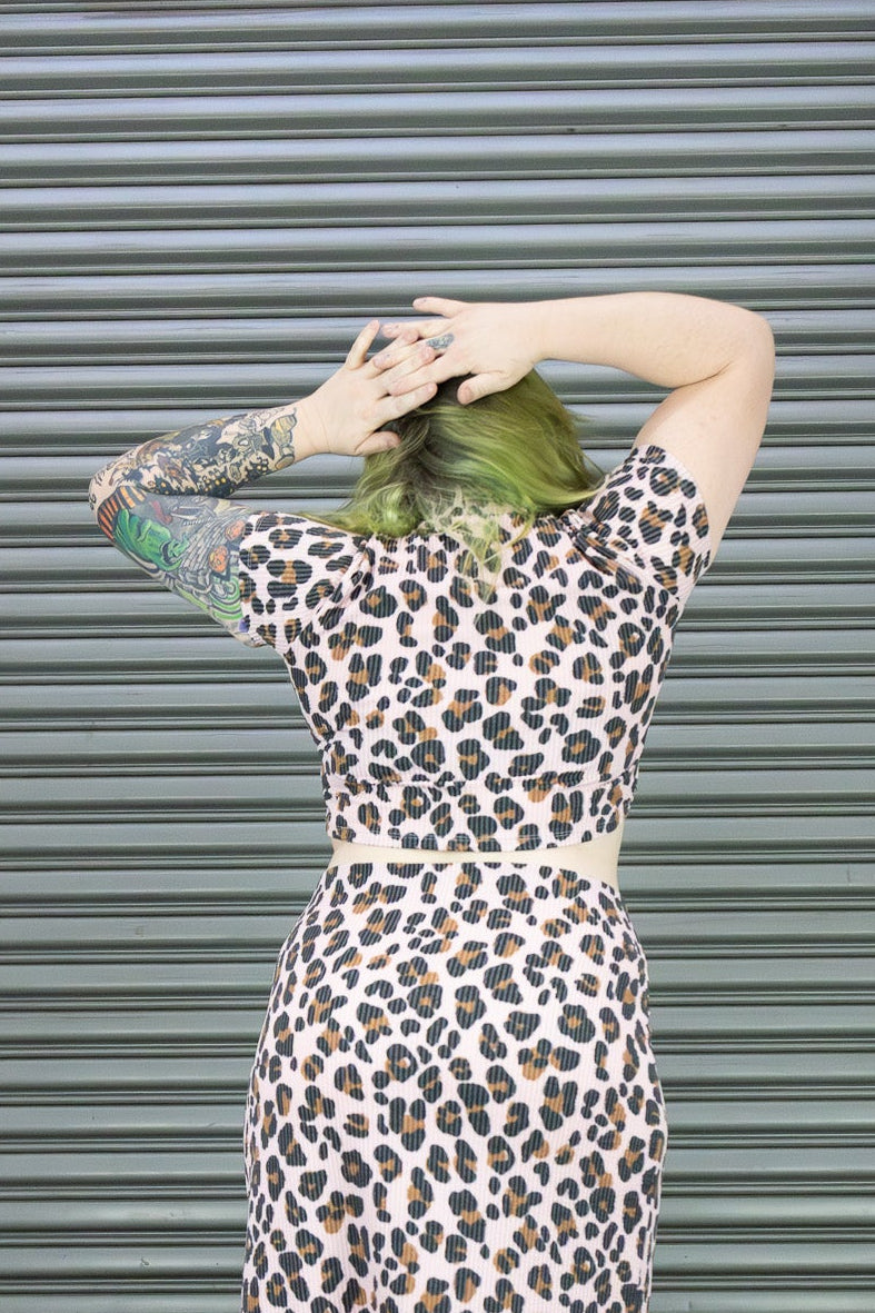 Person wearing a leopard print dress in front of a corrugated metal wall.