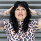 Person wearing a leopard print top with tattoos on arms against a metallic background
