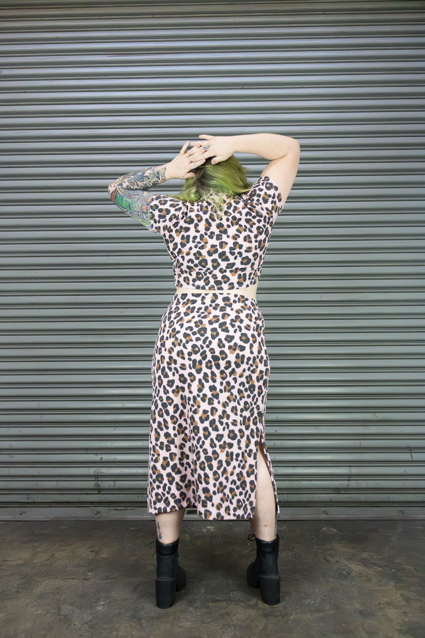 Person wearing a leopard print outfit in front of a corrugated metal wall.