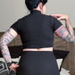 Person wearing a black outfit standing in a bedroom.