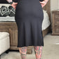 Person wearing a black dress with tattoos on arms and legs in a room.