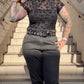 A person wearing a black mesh short sleeve top with a leopard print design, paired with dark jeans and a belt, standing on steps.