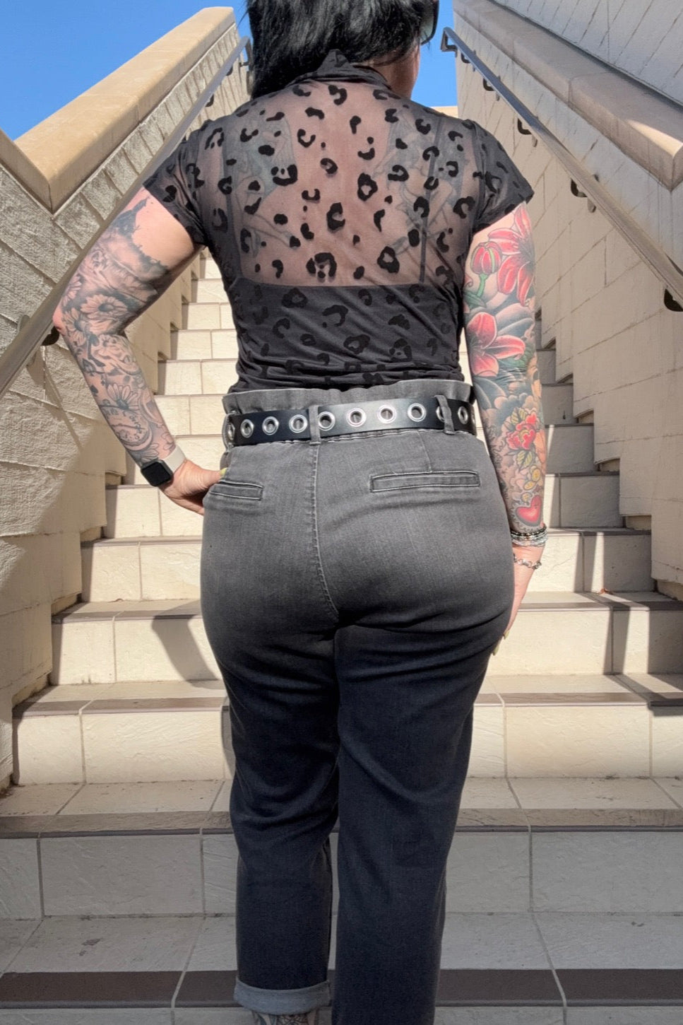 Person wearing a sheer leopard print top and black jeans on a staircase.