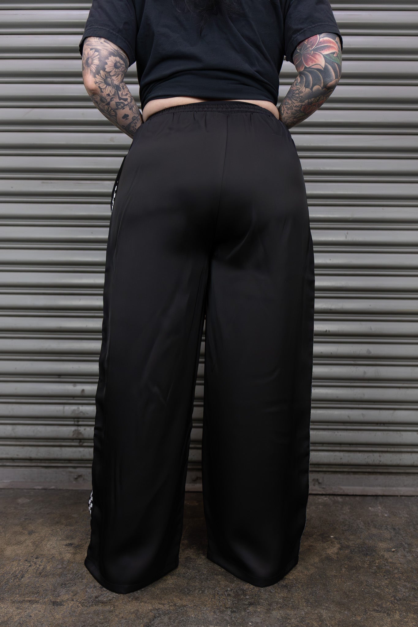 Person wearing black wide-leg pants standing in front of a metallic shutter.