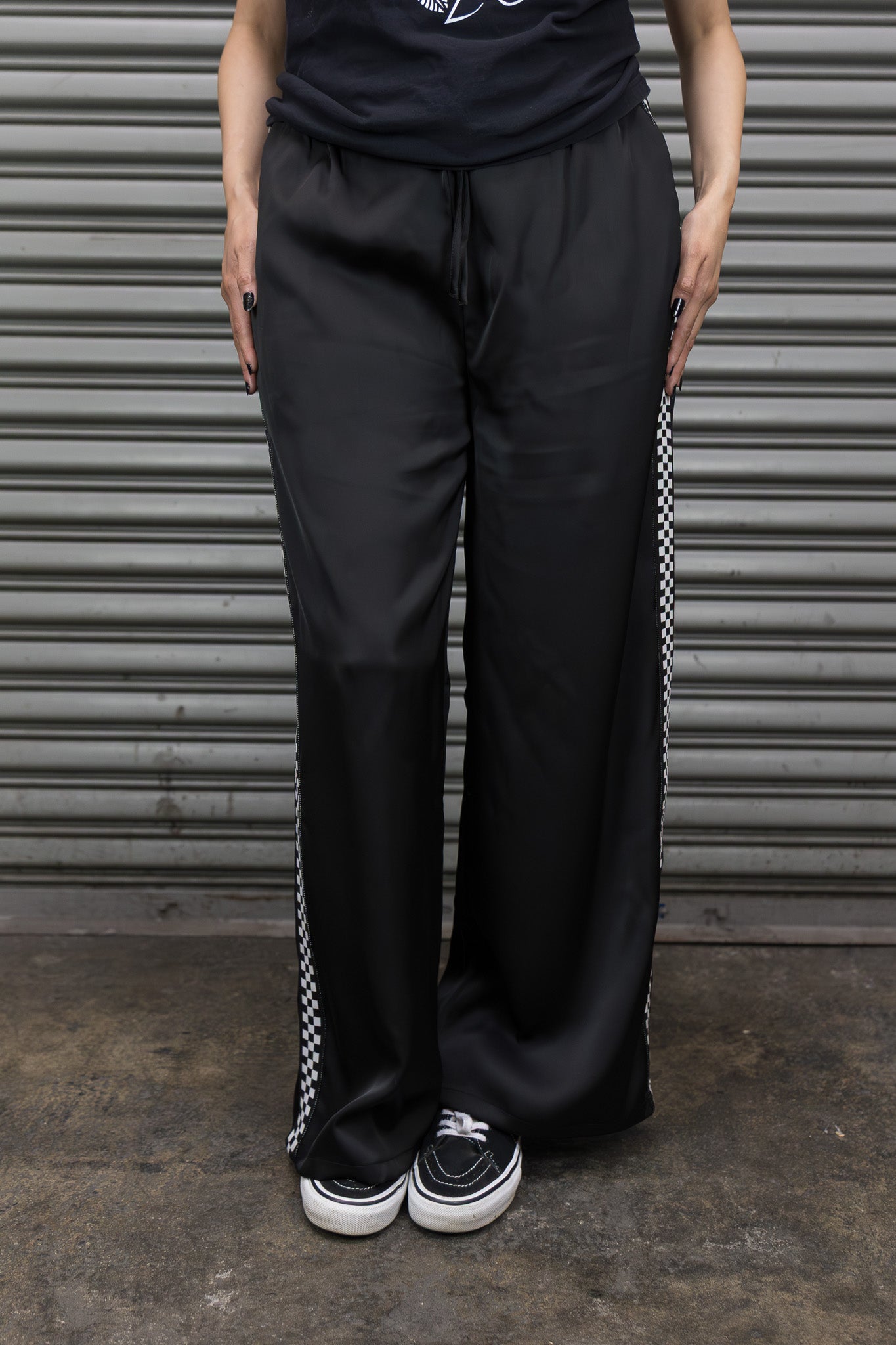 Person wearing black pants with white sneakers in front of a corrugated metal background