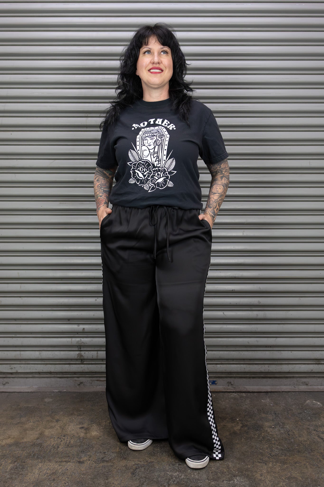 Person wearing a black graphic t-shirt and black pants standing in front of a metal shutter.