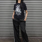 Person wearing a black t-shirt with graphic design and black pants standing in front of a metallic shutter.