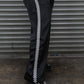 Person wearing black pants with white checkered stripe against a metallic shutter background