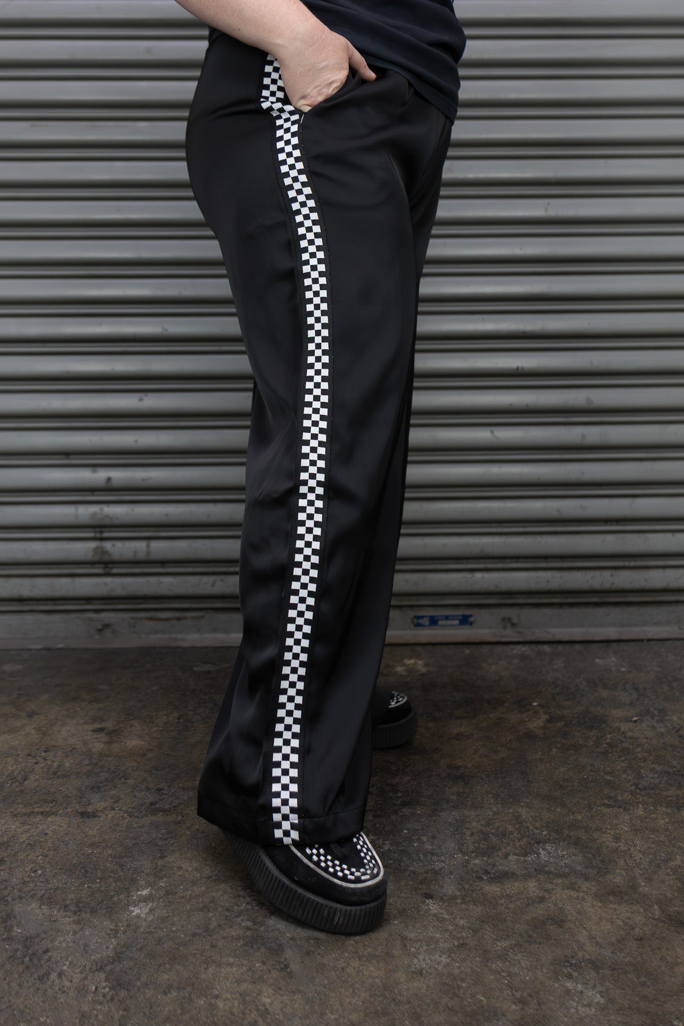 Person wearing black pants with white checkered stripe against a metallic shutter background