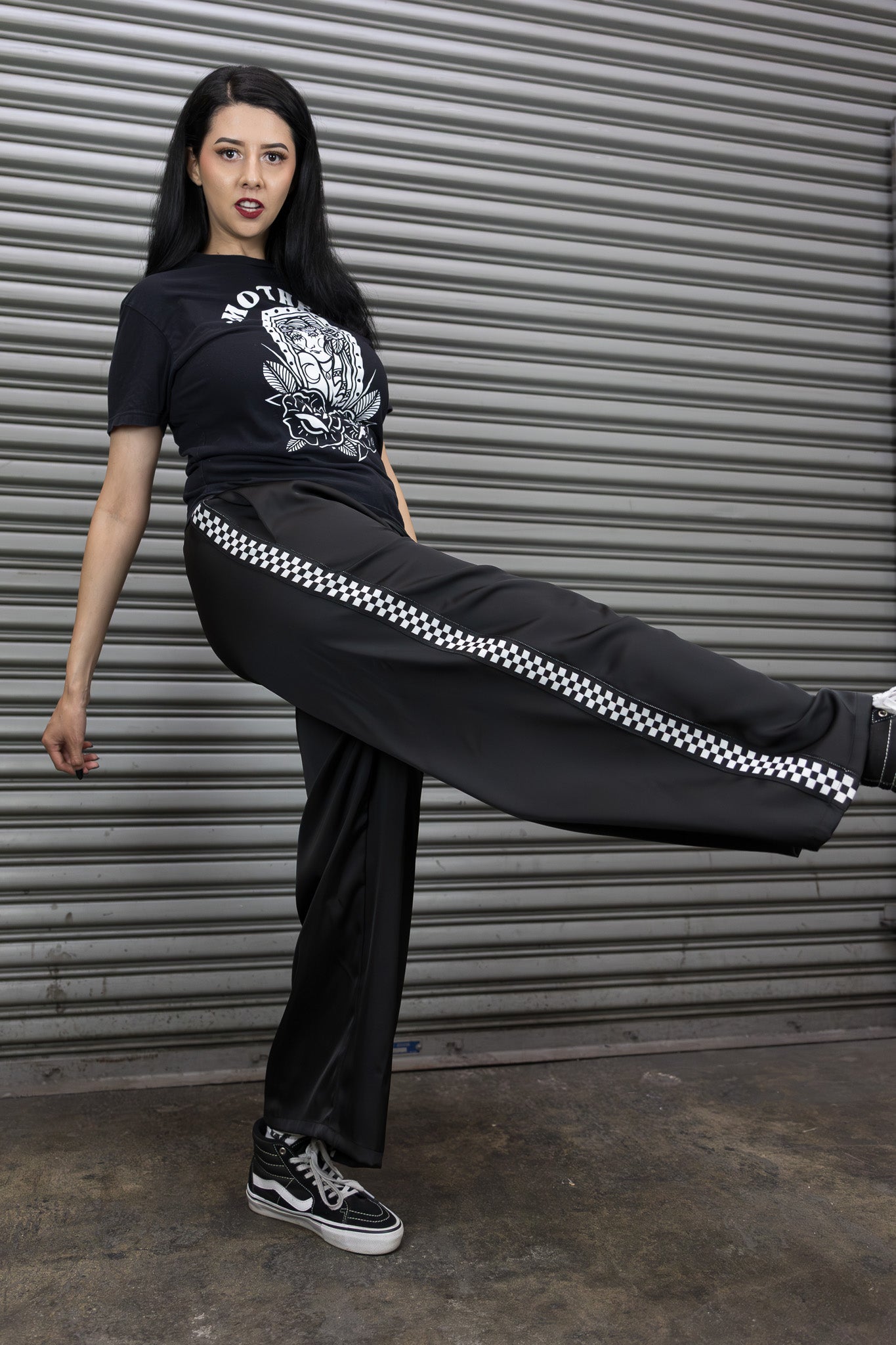Person wearing a black outfit with checkered stripe in front of a metallic shutter.