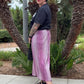 Person wearing a black top and pink pants standing in front of palm trees.