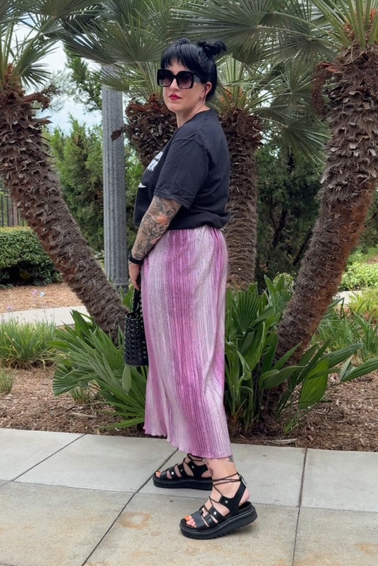 Person wearing a black top and pink pants standing in front of palm trees.