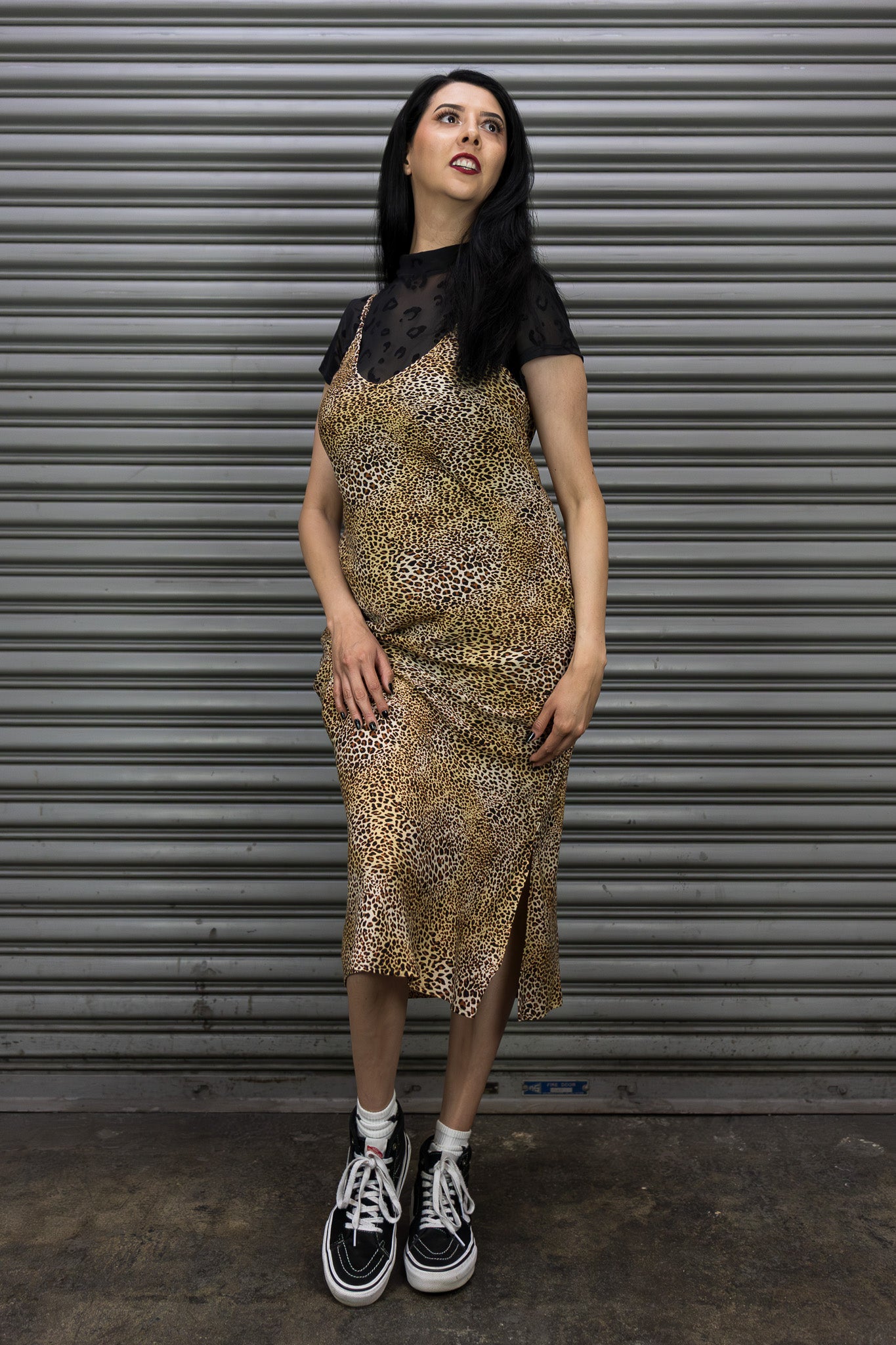 Woman wearing a patterned dress and black sneakers standing in front of a metal shutter.