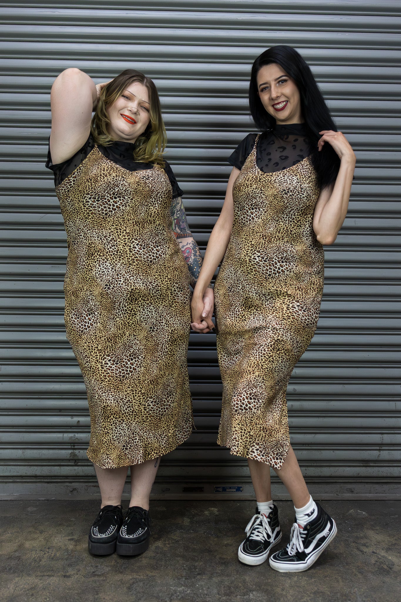 Two women wearing leopard print dresses standing in front of a metal shutter.
