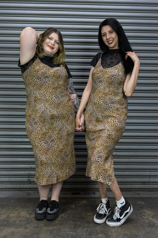 Two women wearing leopard print dresses standing in front of a metal shutter.