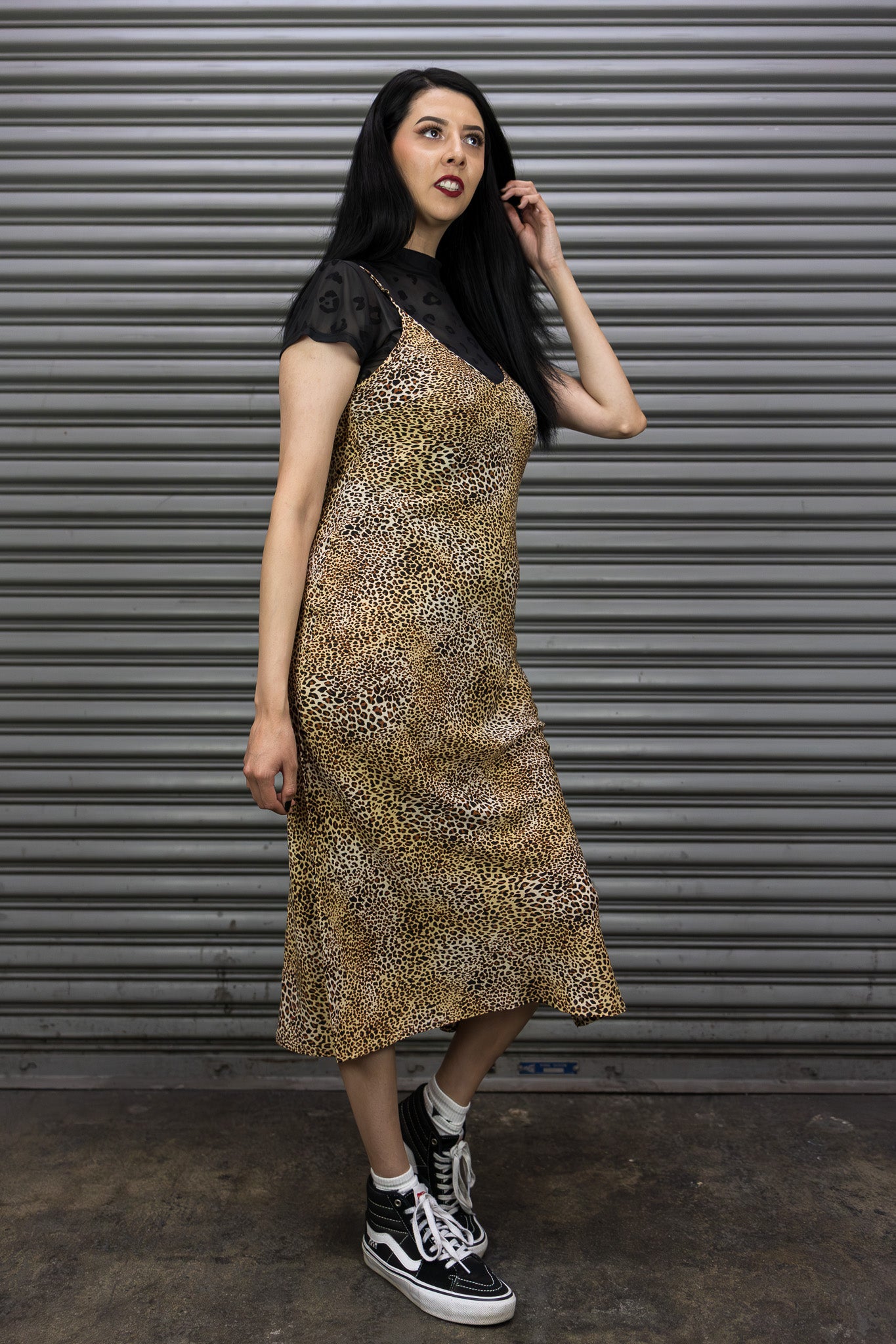 Woman wearing a leopard print dress with black accents against a metallic shutter background
