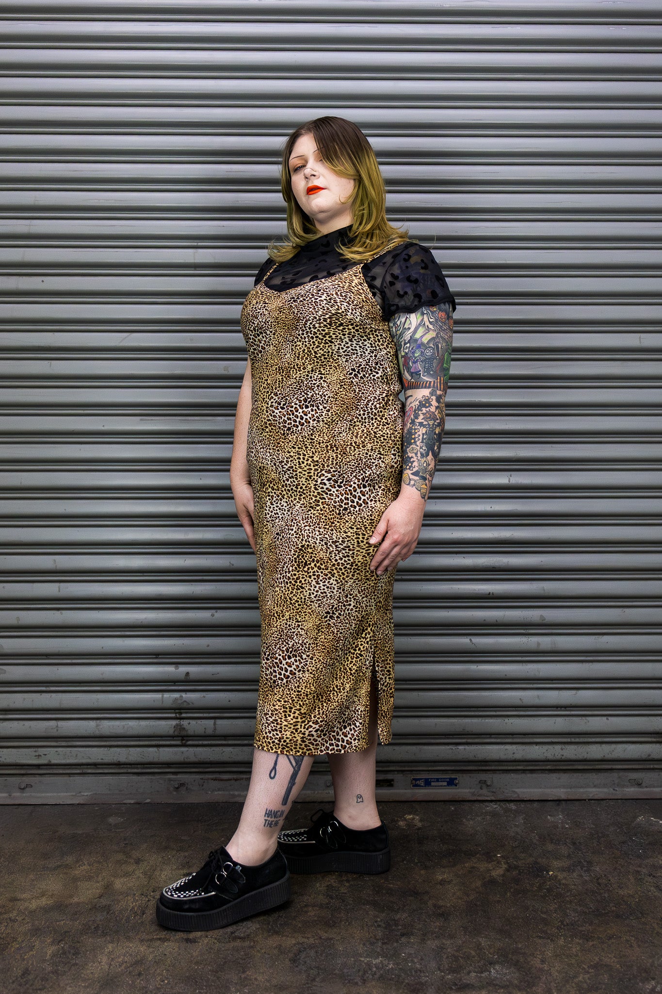 Person wearing a patterned dress with black accents against a metal shutter background