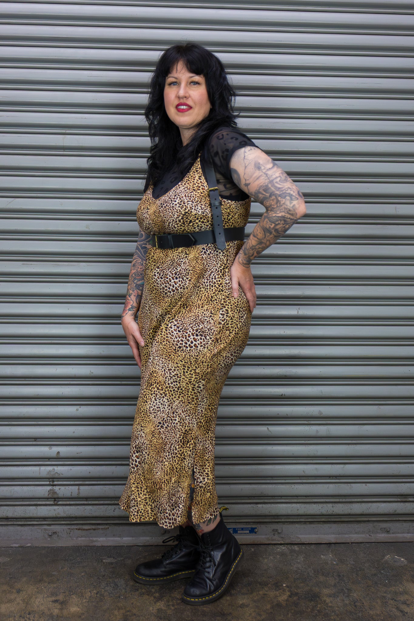 Woman in a leopard print dress standing against a metal shutter.