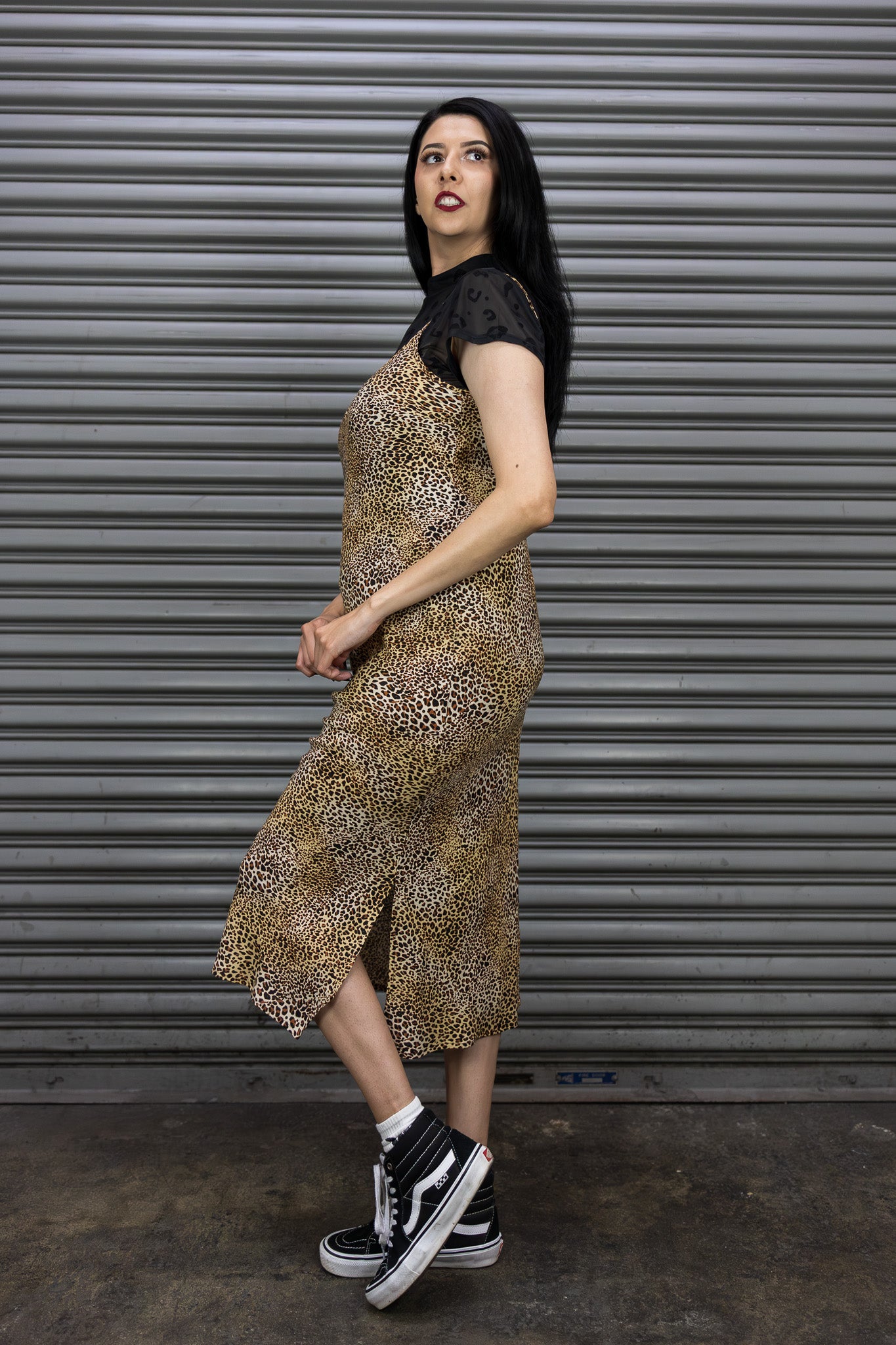 Woman wearing a leopard print dress and black sneakers in front of a metal shutter.