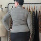 A woman viewed from behind wearing a black and white horizontally striped mock neck top and a black skirt, standing in front of a clothing rack.