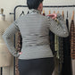 A woman viewed from behind wearing a black and white striped long-sleeve mock neck top and a black skirt, standing in front of a clothing rack.