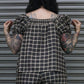 Person wearing a plaid outfit with tattoos visible, standing against a metallic shutter.