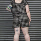 Person wearing a black and white checkered outfit standing in front of a metallic shutter.