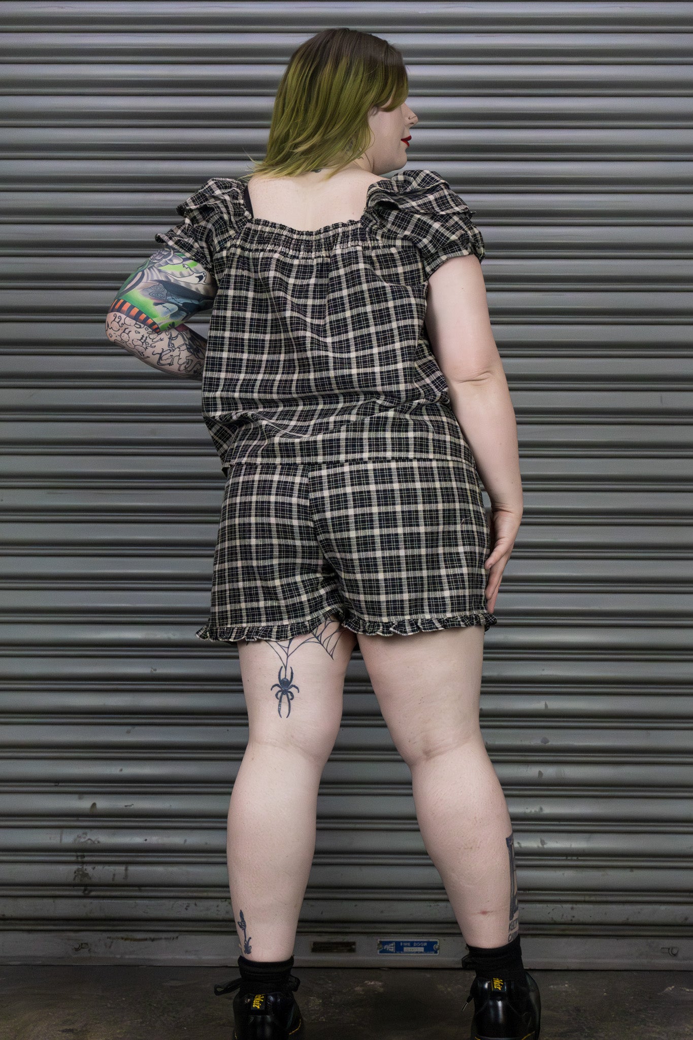 Person wearing a black and white checkered outfit standing in front of a metallic shutter.
