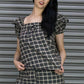 Woman wearing a black and white checkered outfit against a metallic shutter background