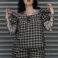 Person wearing a plaid outfit with tattoos standing against a metallic shutter.