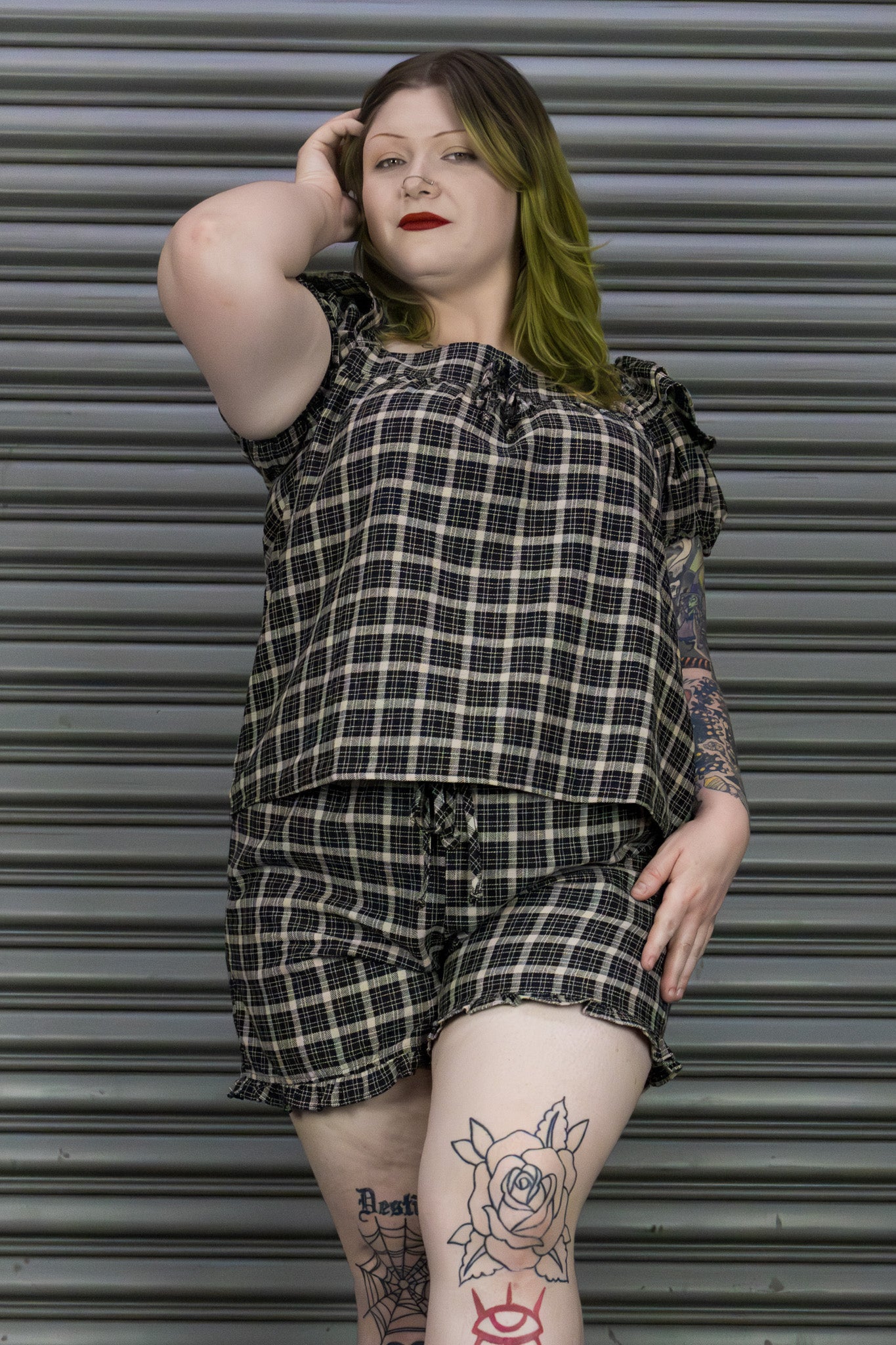 Person wearing a plaid outfit standing in front of a metallic shutter.