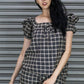 Woman wearing a plaid dress standing in front of a metallic shutter.