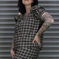 Person wearing a plaid dress with tattoos standing against a metallic shutter.